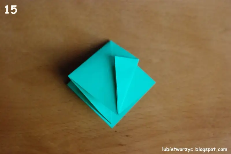 Krok 15 instrukcji, jak zrobić kwadrat z papieru. Turkusowa origami na drewnianym tle.
