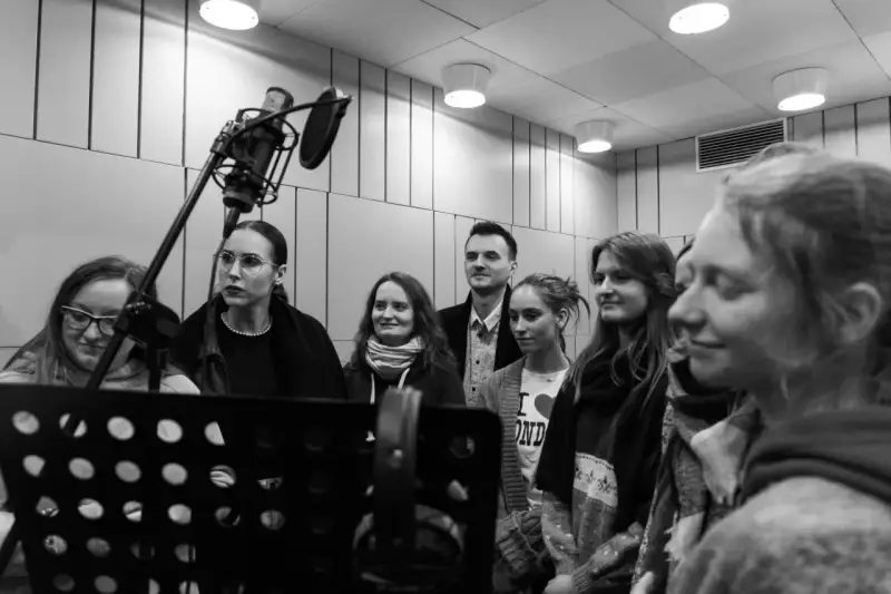 Grupa osób w studiu nagraniowym, przygotowująca podkładanie głosu do bajek. W tle mikrofon studyjny.