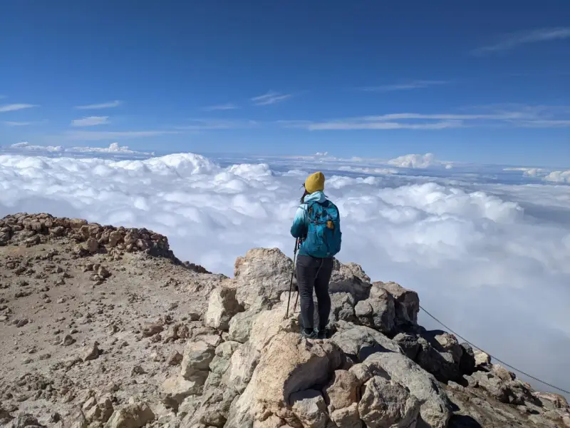 Widok z Teide: turystka w żółtej czapce podziwia morze chmur z wulkanicznego szczytu.